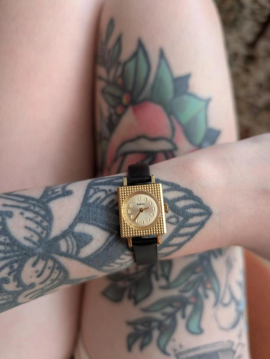 Image of Montre femme à bracelet noir et boîtier doré, cadran clair, sur poignet