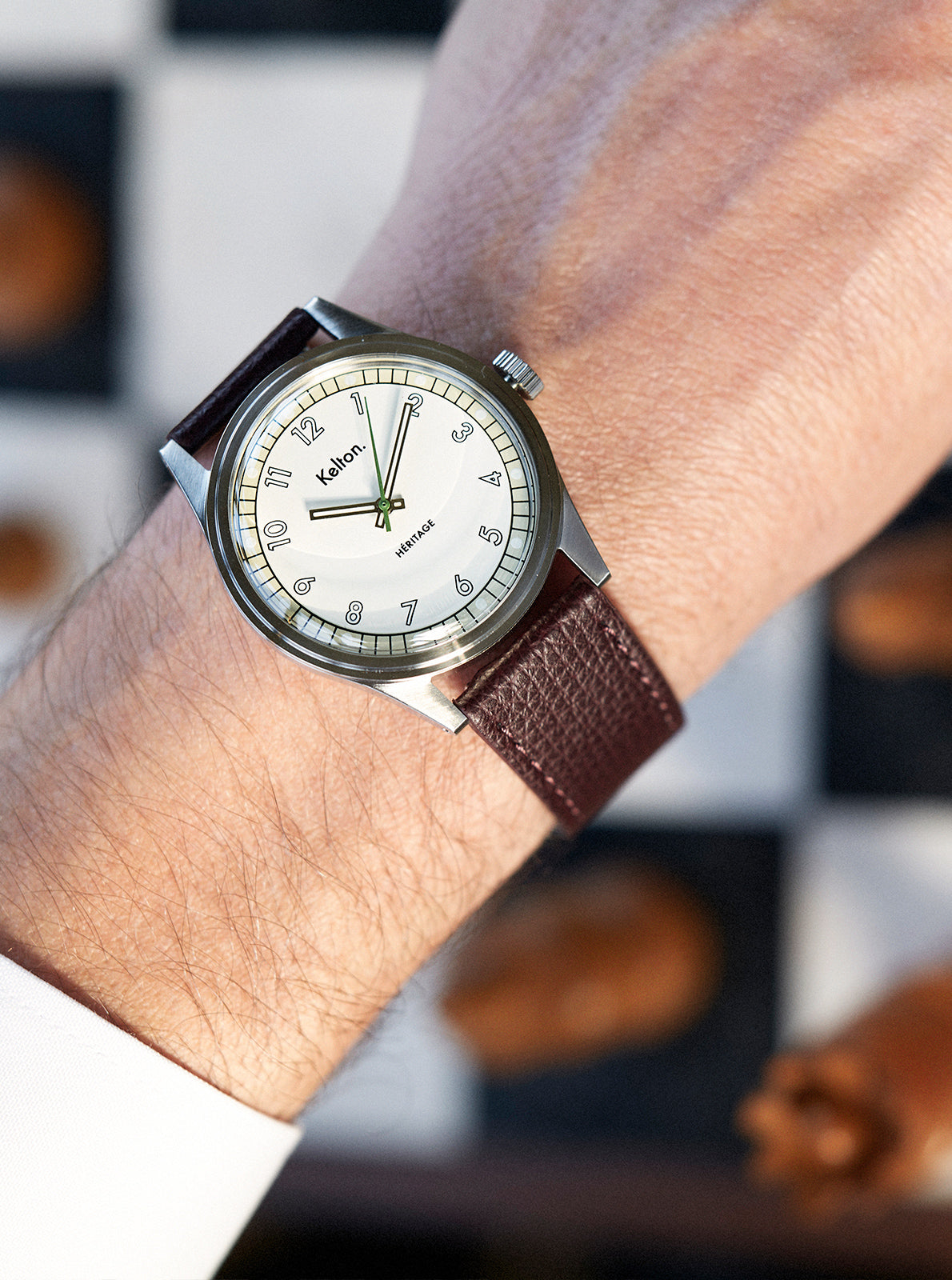 Image of Montre au poignet, cadran clair, bracelet cuir brun foncé, couronne et index visibles