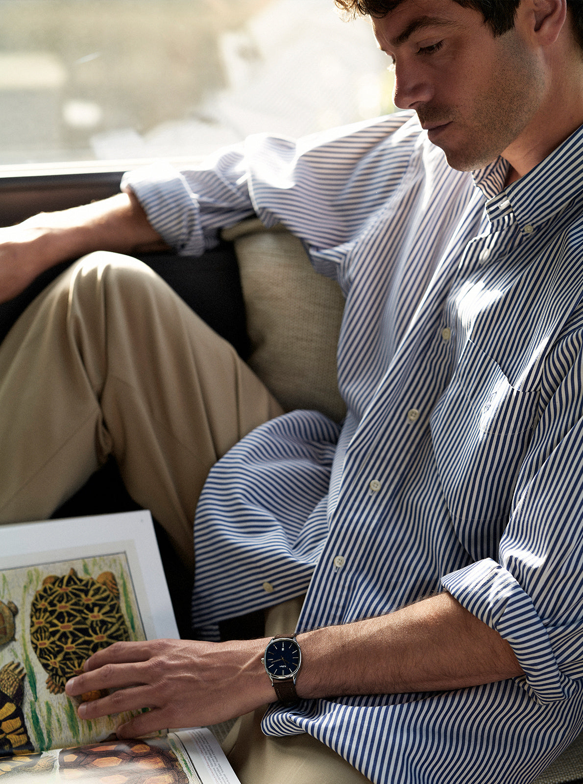 Image of Montre à cadran bleu marine avec bracelet foncé au poignet, homme assis