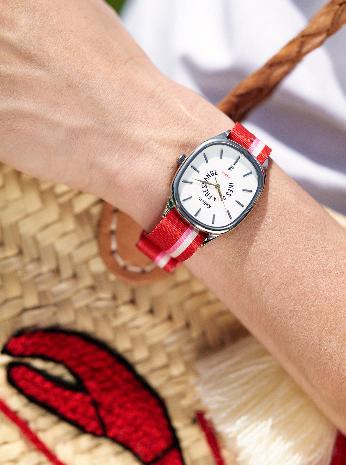 Image of Montre ronde à cadran blanc, bracelet rouge à rayures, vue au poignet.