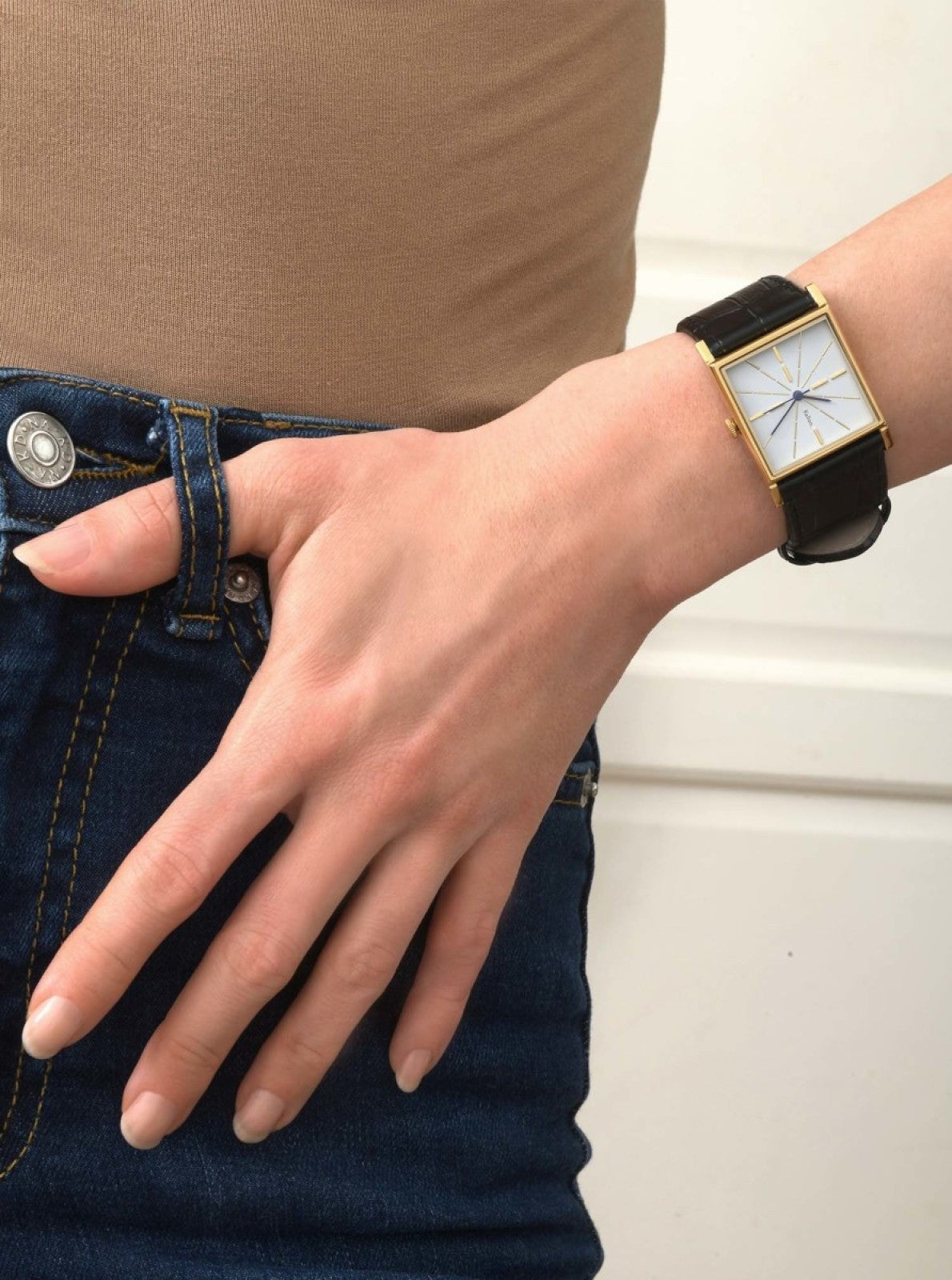 Image of Montre au poignet : boîtier doré carré, cadran blanc et bracelet en cuir noir.