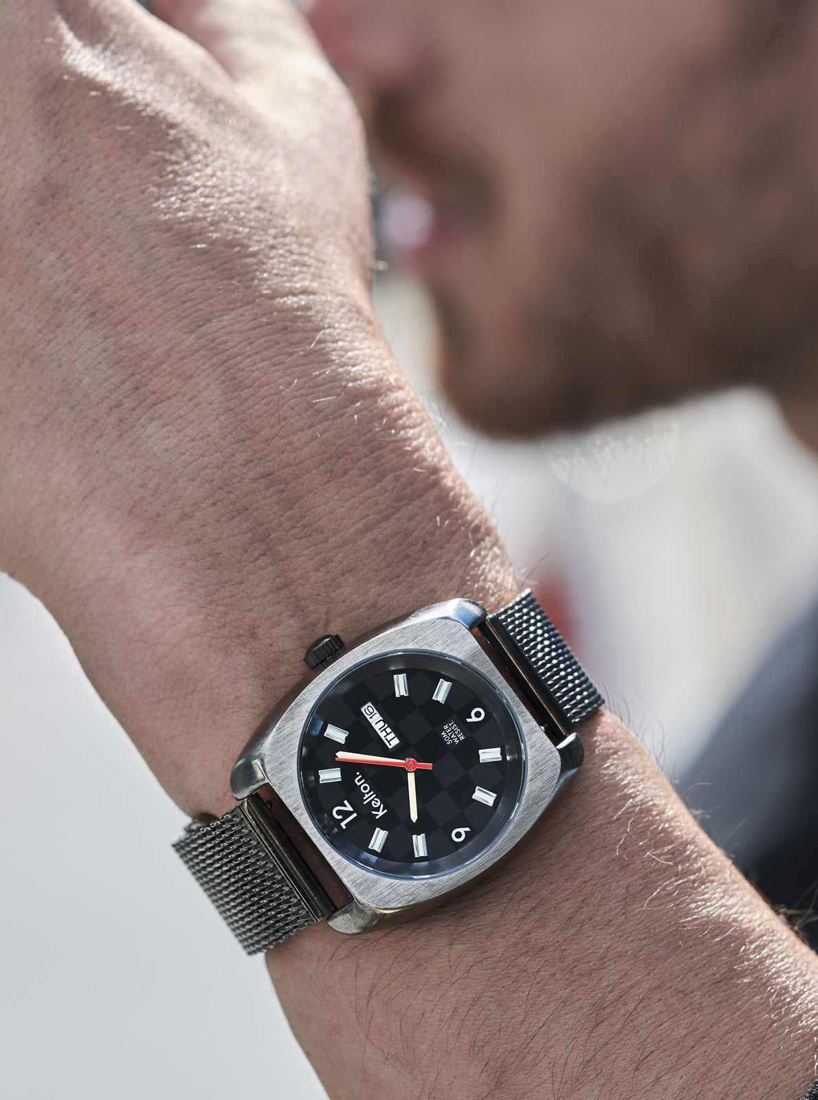 Image of Montre-bracelet noire au poignet, cadran noir et bracelet en maille métallique