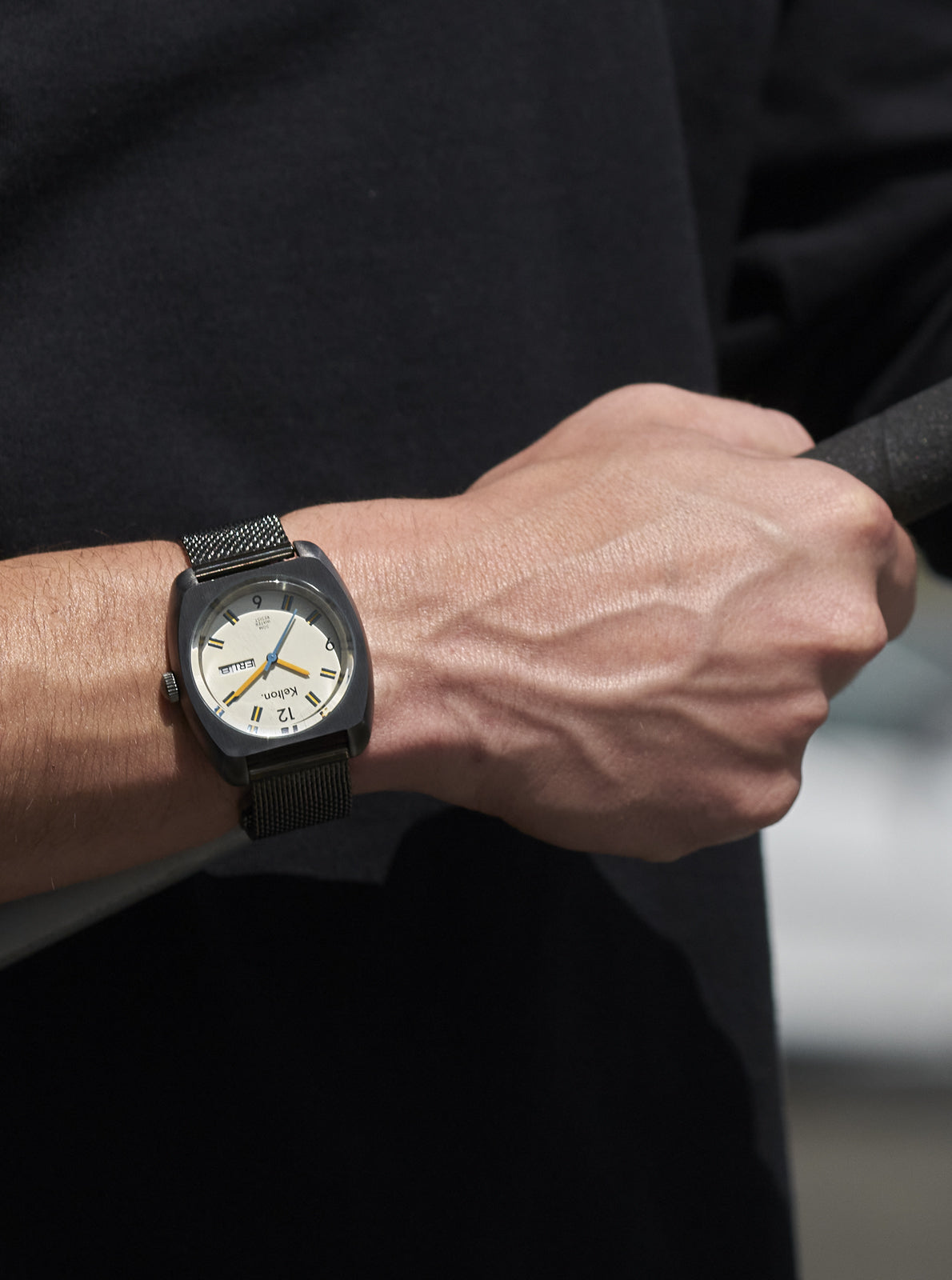 Image of Montre Kelton au poignet, bracelet maille noire et cadran crème, index jaunes